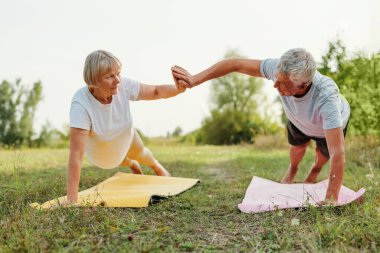 Parkta aktif yaşlı bir çift, beşlik çakıyor, takım çalışması yapıyor ve sağlıklı bir yaşam tarzı sergiliyor..