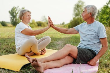 Yoga minderleri üzerinde aktif yaşlı bir çift parkta beşlik çakıyor..
