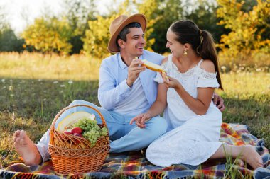 Piknik battaniyesinde bir dilim kavunu paylaşan ve birbirlerine gülümseyen sevgi dolu bir çift..