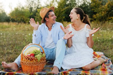 Gülen bir çift piknikten zevk alıyor. Elleriyle bir anlık neşeyi paylaşırken işaret ediyorlar..