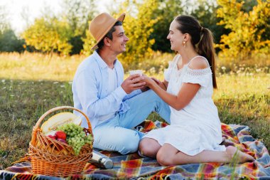 Romantik piknikten zevk alan genç bir çift, birlikte çay içip birbirlerine gülümsüyorlar..