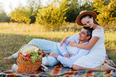 Tarlada piknik yapan romantik genç bir çift. Kadın, adamı kucağında yatarken arkadan kucaklıyor..