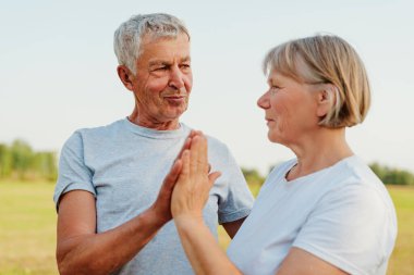 Elleri dua ederken çimen tarlasında birbirlerine bakan olgun bir çift..
