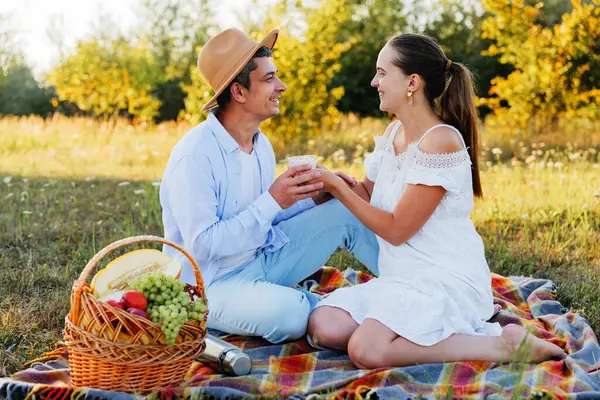Romantik piknikten zevk alan genç bir çift, birlikte çay içip birbirlerine gülümsüyorlar..