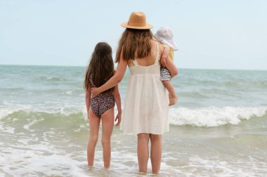 Üç aile ferdi sıcak suda oynayarak deniz kenarında güneşli bir yaz gününde neşeli anılar yaratıyor.