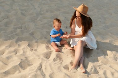 Güneşli bir sahil gününde bir anne ve küçük oğlunun kumsalda oynayıp kahkahalarını paylaşırken neşeli bir an yaşanıyor..