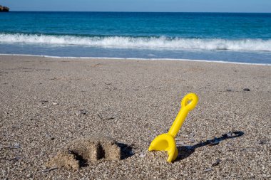 Arka planda turkuaz deniz bulunan bir kumsalda bırakılmış sarı plastik kürek yaz tatili için mükemmel.