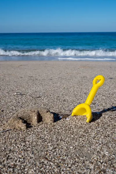 Arka planda turkuaz deniz bulunan bir kumsalda bırakılmış sarı plastik kürek yaz tatili için mükemmel.