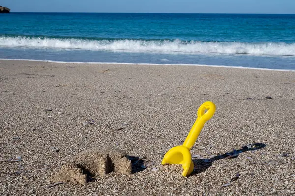 Arka planda turkuaz deniz bulunan bir kumsalda bırakılmış sarı plastik kürek yaz tatili için mükemmel.