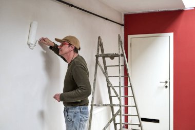 Kirli elbiseli bir ressam çatı katındaki bir duvarı yeniliyor.