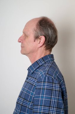 Beyaz duvara karşı pamuklu gömlekli yaşlı adam.