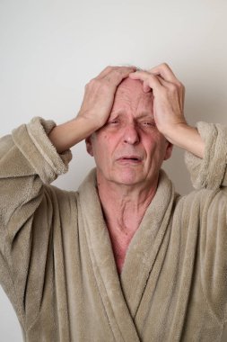 Yaşlı adam bej bornoz ve dağınık saç kamera önünde çirkin bir yüz yapar.