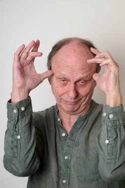 Yeşil gömlekli yaşlı adam kameranın önünde çirkin bir yüz ifadesi takın.