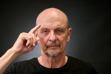 Stüdyoda eski bir Harcourt tarzı ışıklandırmada selam veren yaşlı bir adamın yakın plan portresi