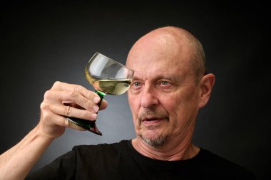 Eski bir Harcourt tarzı ışıklandırmayla iyi bir beyaz şarabın tadına bakan yaşlı bir adamın yakın plan portresi.