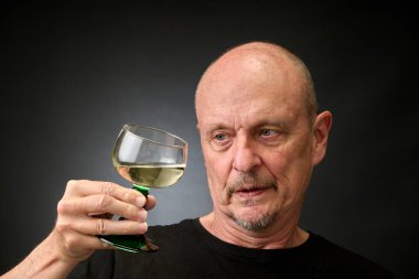 Eski bir Harcourt tarzı ışıklandırmayla iyi bir beyaz şarabın tadına bakan yaşlı bir adamın yakın plan portresi.