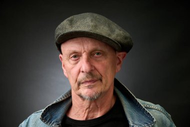 Eski bir Harcourt tarzı ışıklandırması olan şapkalı ve kot ceketli son sınıf bir adamın yakın plan portresi.