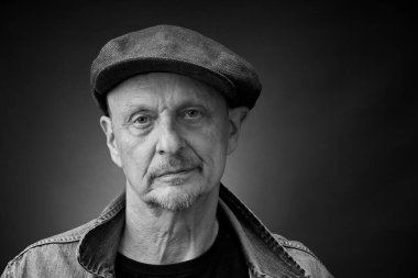 Tek renkli kapanış portresi, eski bir Harcourt tarzı ışıklandırmada, kep ve kot ceket giyen son sınıf bir adamın resmi.