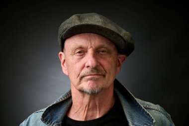 Eski bir Harcourt tarzı ışıklandırması olan şapkalı ve kot ceketli son sınıf bir adamın yakın plan portresi.