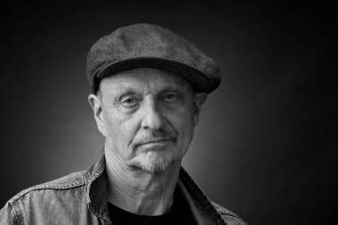 Tek renkli kapanış portresi, eski bir Harcourt tarzı ışıklandırmada, kep ve kot ceket giyen son sınıf bir adamın resmi.