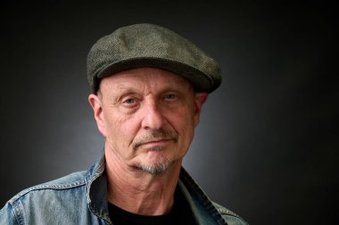 Eski bir Harcourt tarzı ışıklandırması olan şapkalı ve kot ceketli son sınıf bir adamın yakın plan portresi.