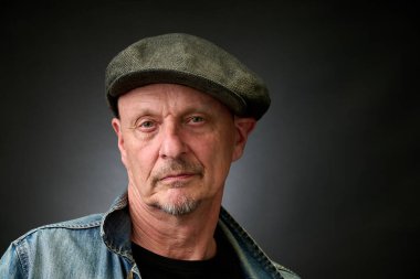 Eski bir Harcourt tarzı ışıklandırması olan şapkalı ve kot ceketli son sınıf bir adamın yakın plan portresi.