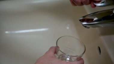 Adamın biri bardağı lavabodan suyla dolduruyor..