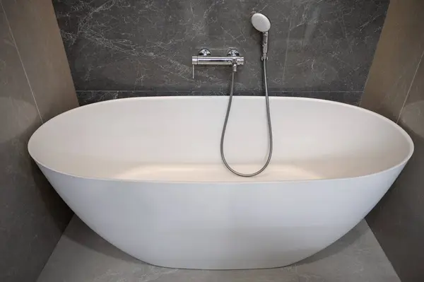 Minimalist banyo. Beyaz banyo küveti ve gümüş telefonlar duş alıyor.