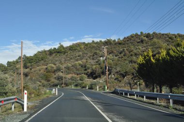 Asfalt bir yol dağların ve ağaçların arasından geçer.