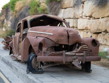 Paslı, terk edilmiş, ağır hasar görmüş, kaldırıma park edilmiş eski bir araba.