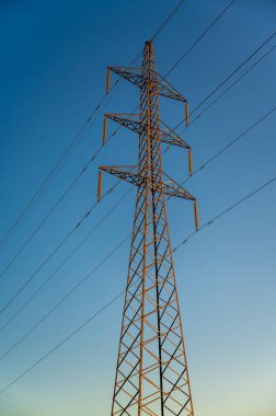 Bu, günbatımında elektrik hattı pilonu olarak da bilinen yüksek voltajlı bir elektrik iletim kulesinin görüntüsü.