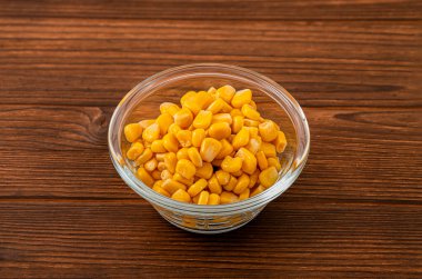 Glass bowl filled with vibrant yellow corn kernels on a rustic wooden background, showcasing a fresh and appetizing close-up of this healthy vegetable clipart