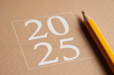 2025 kahverengi günlük, ahşap masanın üstünde kalem var.