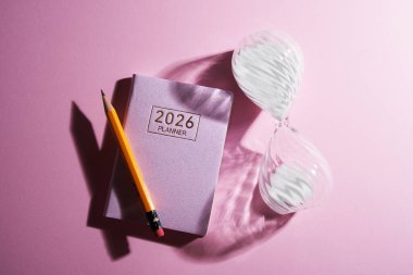 2026 küçük planlayıcı, kum saati ve kalem pembe arka plana karşı.