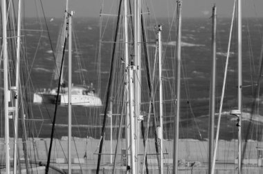 İtalya, Sicilya, Akdeniz, Marina di Ragusa (Ragusa Eyaleti); limanda yelkenli direkleri ve arka planda bir yelkenli teknesi 