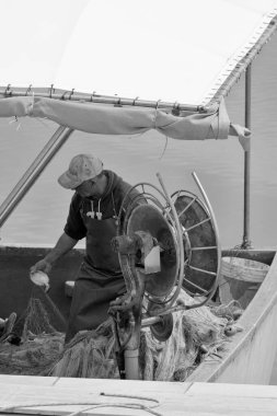 İtalya, Sicilya, Akdeniz, Marina di Ragusa (Ragusa Eyaleti); limandaki balıkçı teknesinde balıkçı ağlarını temizleyen yerel balıkçı 