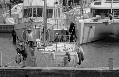 İtalya, Sicilya, Akdeniz, Marina di Ragusa (Ragusa Eyaleti); 24 Mayıs 2023, limanda bir yelkenli teknesi ve lüks yatlarda bir çift - EDITORIAL