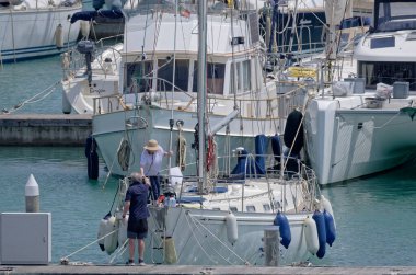 İtalya, Sicilya, Akdeniz, Marina di Ragusa (Ragusa Eyaleti); 24 Mayıs 2023, limanda bir yelkenli teknesi ve lüks yatlarda bir çift - EDITORIAL