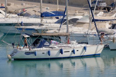 İtalya, Sicilya, Akdeniz, Marina di Ragusa (Ragusa Eyaleti); 7 Temmuz 2023, limandaki bir yelkenli ve lüks yatlarda erkekler - EDITORIAL