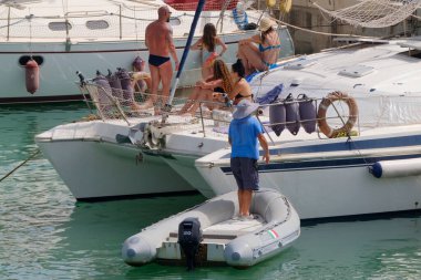 İtalya, Sicilya, Akdeniz, Marina di Ragusa (Ragusa ili); 9 Temmuz 2023, limandaki bir yelkenli teknesinde insanlar - EDITORIAL