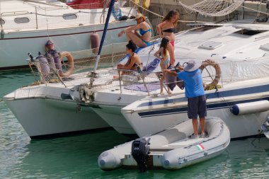 İtalya, Sicilya, Akdeniz, Marina di Ragusa (Ragusa ili); 9 Temmuz 2023, limandaki bir yelkenli teknesinde insanlar - EDITORIAL