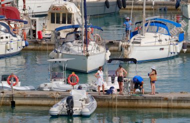 İtalya, Sicilya, Akdeniz, Marina di Ragusa (Ragusa Eyaleti); 9 Temmuz 2023, limandaki bir yelkenli ve lüks yatlarda erkekler - EDITORIAL