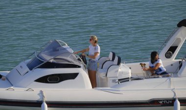 İtalya, Sicilya, Akdeniz, Marina di Ragusa (Ragusa Eyaleti); 1 Eylül 2023, limandaki büyük bir kauçuk teknede köpeği olan kadınlar - EDITORIAL