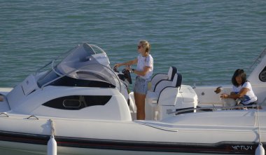 İtalya, Sicilya, Akdeniz, Marina di Ragusa (Ragusa Eyaleti); 1 Eylül 2023, limandaki büyük bir kauçuk teknede köpeği olan kadınlar - EDITORIAL