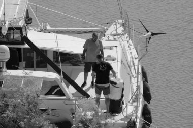 İtalya, Sicilya, Akdeniz, Marina di Ragusa (Ragusa Eyaleti); 4 Eylül 2021, limandaki bir katamaran yelkenli teknesinde erkekler - EDITORIAL