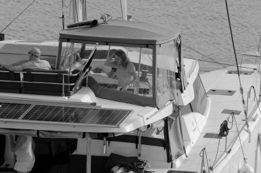 İtalya, Sicilya, Akdeniz, Marina di Ragusa (Ragusa Eyaleti); 9 Kasım 2023, limandaki katamaran yelkenli teknesindeki insanlar - EDITORIAL