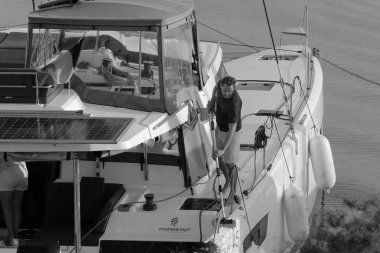 İtalya, Sicilya, Akdeniz, Marina di Ragusa (Ragusa Eyaleti); 9 Kasım 2023, limandaki bir katamaran yelkenli teknesinde adam - EDITORIAL