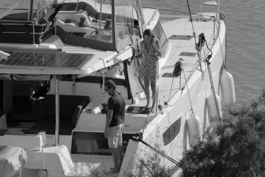 İtalya, Sicilya, Akdeniz, Marina di Ragusa (Ragusa Eyaleti); 11 Kasım 2023, limanda bir katamaran yelkenli teknesinde çift - EDITORIAL