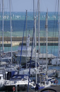 İtalya, Sicilya, Akdeniz, Marina di Ragusa (Ragusa Eyaleti); 11 Şubat 2024, limanda lüks yatlar ve denizde yelkenli yarışı - EDITORIAL