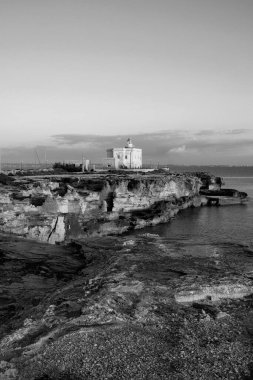 İtalya, Sicilya, Akdeniz, Egadi takımadaları, Favignana Adası (Trapani Eyaleti); gün batımında bir deniz feneri ve adanın kayalık sahili manzarası